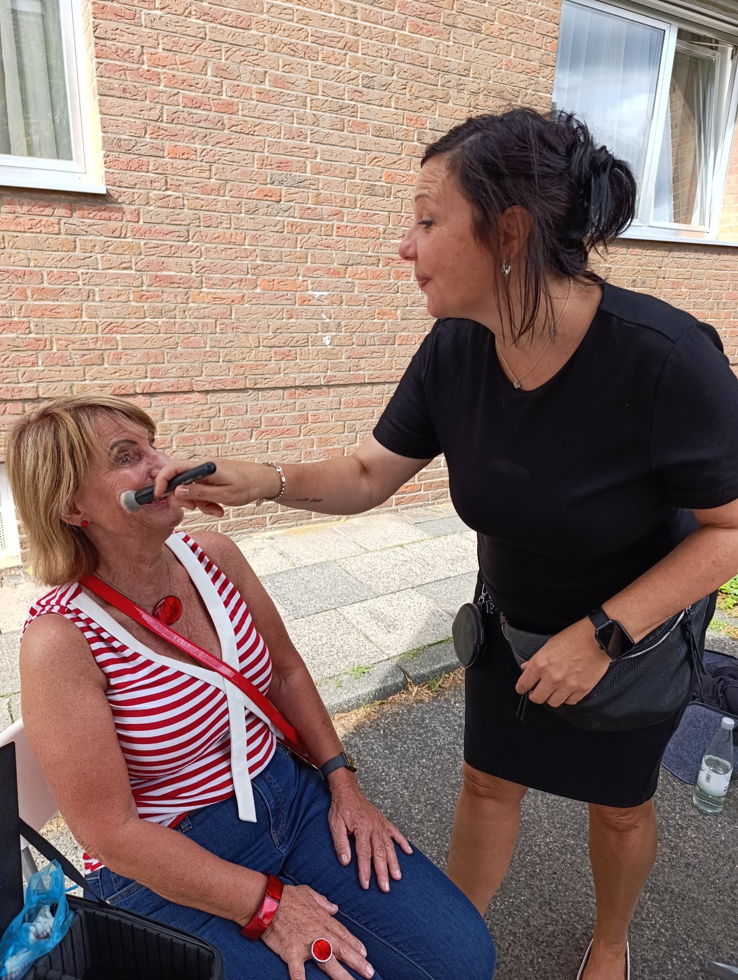Nicole Christandl schminkt eine Kundin im Freien und setzt mit einem Pinsel Farbe an der Wange an