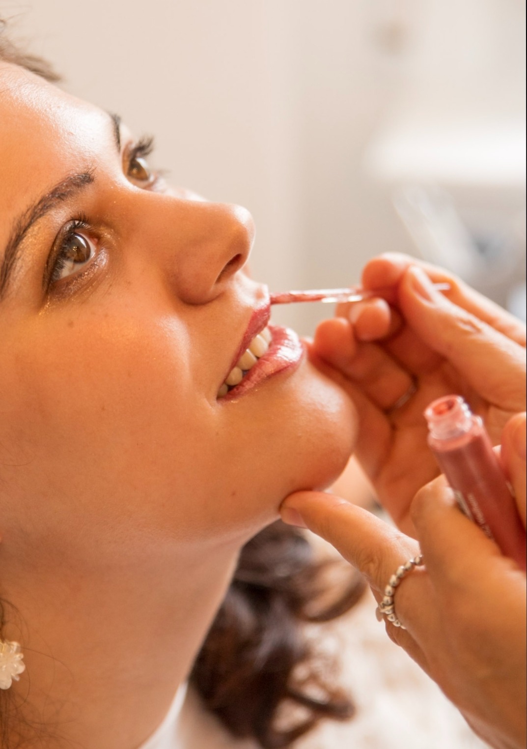 Detailaufnahme: rosafarbener Lipgloss wird mit einem Applikator auf die Lippen einer Braut aufgetragen