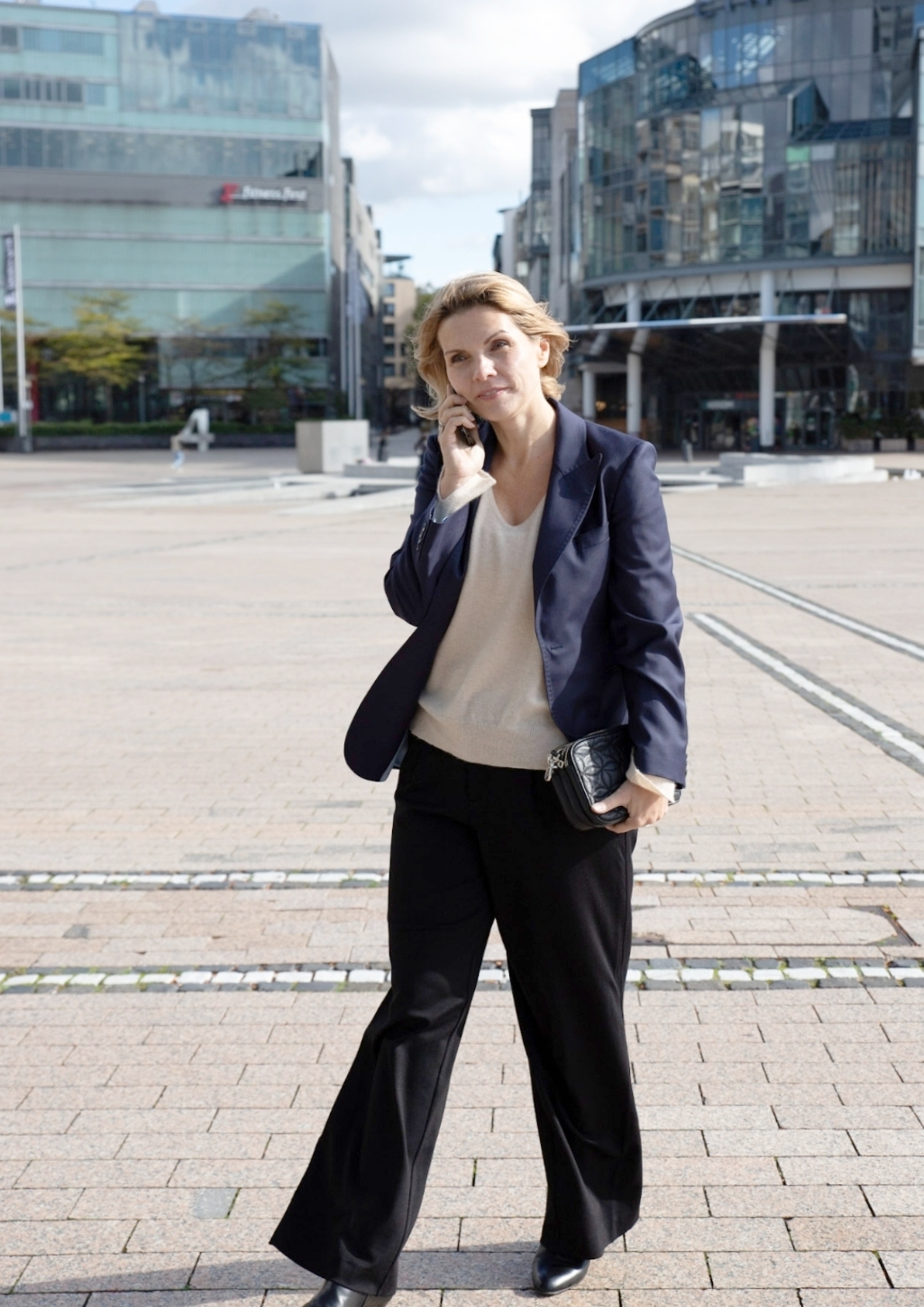 Frau in Blazer und cremefarbenem Pullover mit Business-Make-up auf einem Stadtplatz