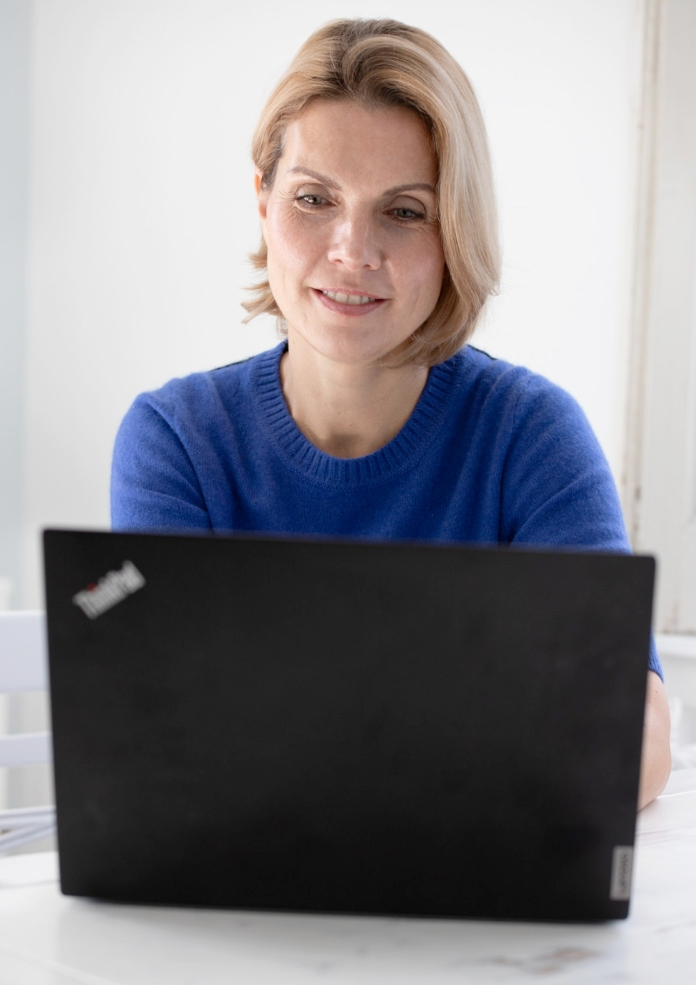 Frau mit dezentem Business-Make-up und blauem Pullover hinter einem Laptop